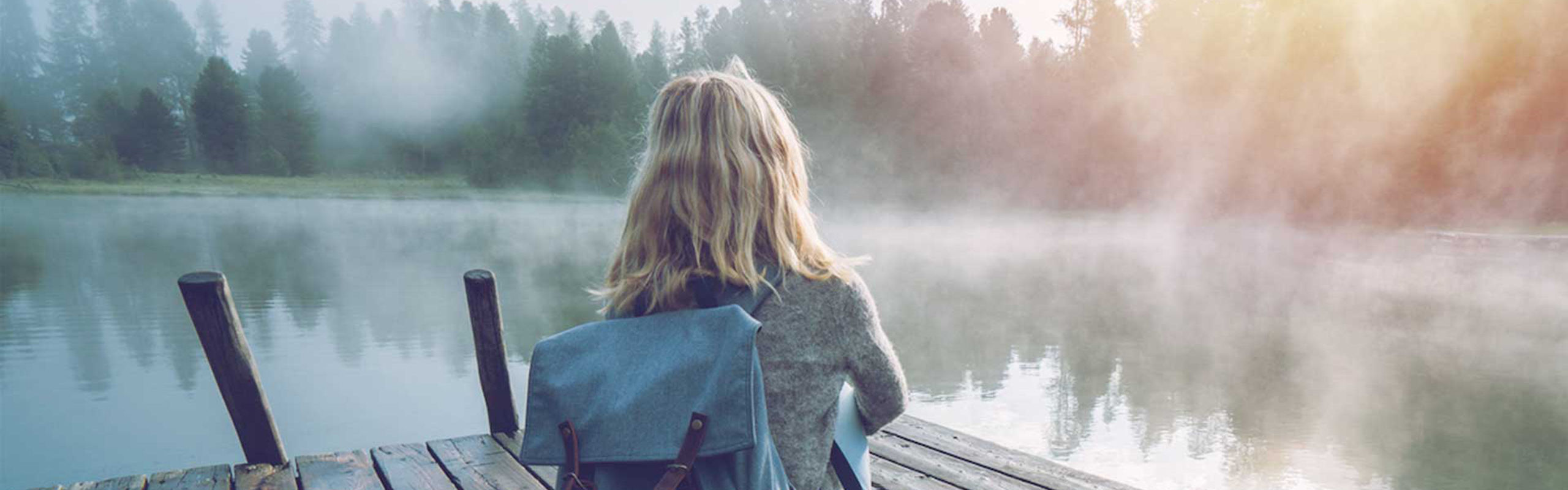 Bild einer Frau die auf einem Steg an einem See sitzt